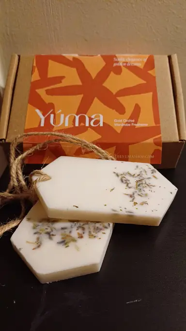 Two white YUMA Gold Orchid wardrobe sachets with dried flowers in front of their packaging.