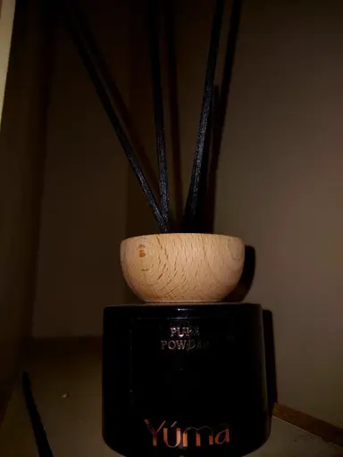 YUMA black room diffuser with a wooden cap and black reeds against a dark background.