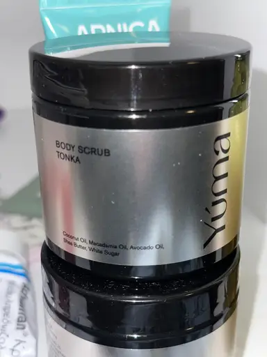 YUMA Tonka Body Scrub metallic jar with a black lid, placed on top of its packaging.