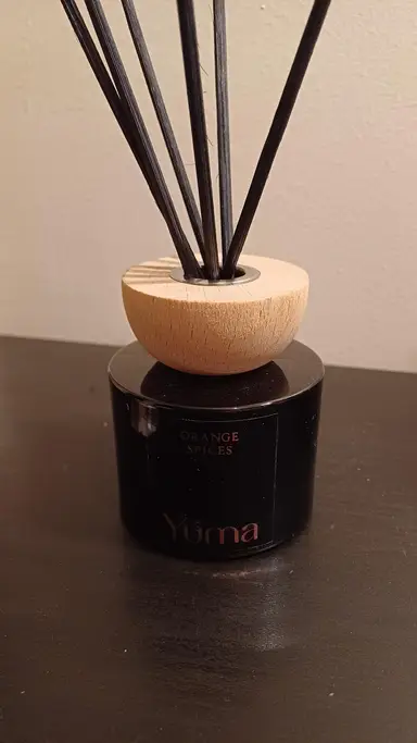 YUMA black glass room diffuser with a wooden cap and black reeds on a dark surface.