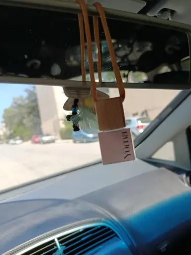 A YUMA car freshener with a wooden cap hanging from a vehicle's rearview mirror.