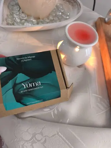 A Yúma SCENT DISCOVERY KIT box next to a lit white burner with pink melted wax.