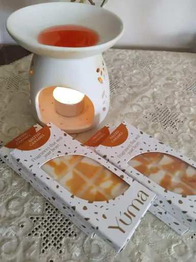 White ceramic wax burner with a lit tea light and melted wax, next to YUMA Salted Caramel wax melt packaging.