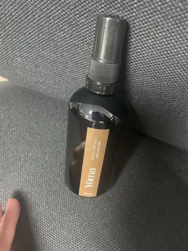 YUMA Gold Orchid Room Mist black bottle on a grey fabric surface.