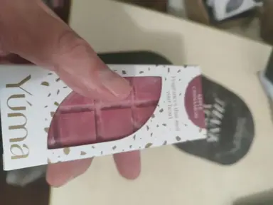 A hand holding a white YUMA box containing pink chocolate-shaped wax melts.