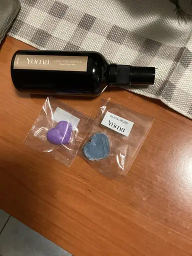A black YUMA room spray bottle next to two heart-shaped scented candles.