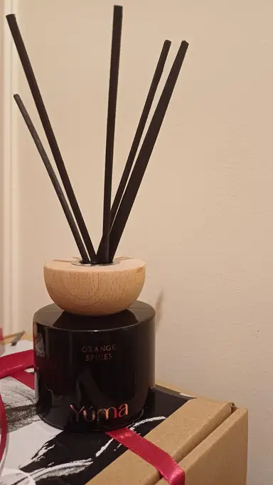 A black glass YUMA reed diffuser with a wooden lid and black reeds, Orange Spices scent.
