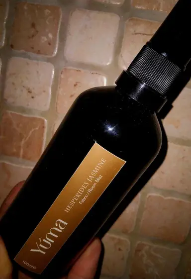 YUMA Hesperides Jasmine Room Mist in a dark bottle with a gold label, placed on a stone surface.