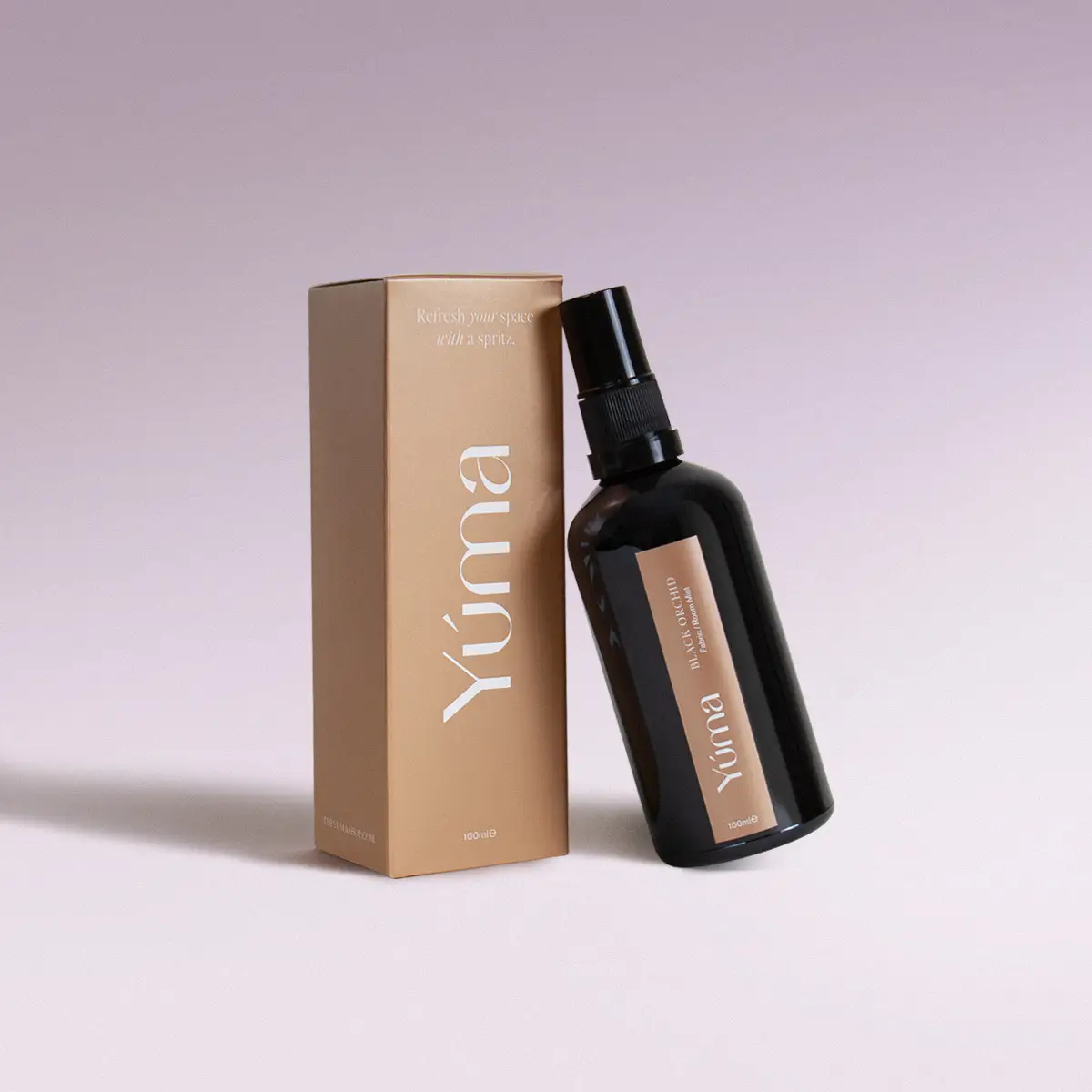 YUMA Black Orchid fabric mist in a black bottle next to its beige paper packaging.