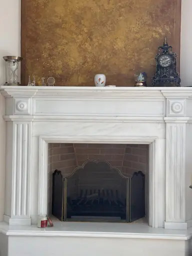 White marble fireplace with decorative objects, a YUMA candle, and a gold-effect wall design.