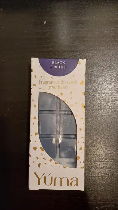 YUMA Black Orchid blue wax melt in white packaging with gold details, on a dark surface.