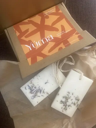 Two white wardrobe sachets with dried flowers beside the YUMA Gold Orchid paper packaging.
