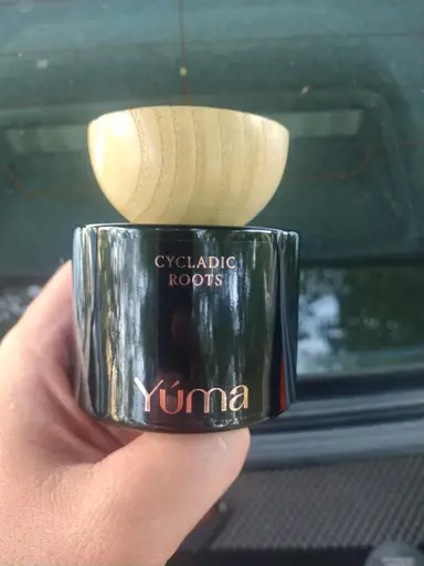 A hand holding the YUMA Cycladic Roots black glass jar with a wooden lid.