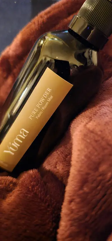 YUMA Room Mist Pure Powder dark glass bottle placed on soft brown fabric.