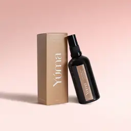 Dark glass bottle of Pure Powder Fabric/Room Mist beside its paper packaging on a pink background.