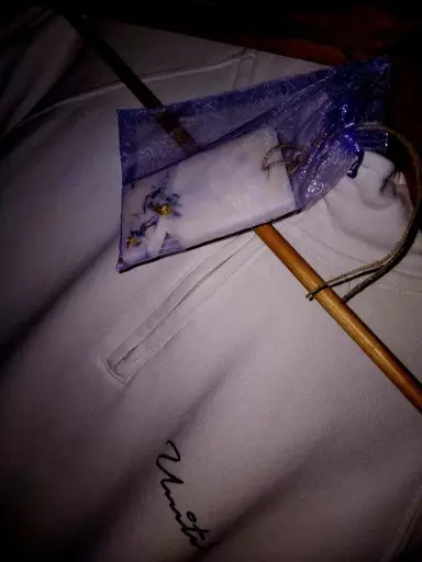 A rectangular wardrobe sachet with dried flowers inside a purple organza pouch on a wooden hanger.