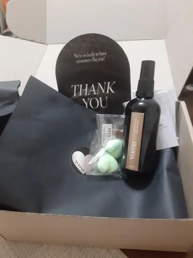 Open white box with a black spray bottle, a pouch containing green items, and a thank-you card.