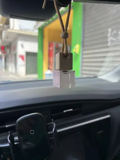 A small glass YUMA car fragrance bottle with a wooden cap hanging from a rearview mirror.