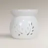White ceramic wax melt burner with a perforated leaf design on a light background.