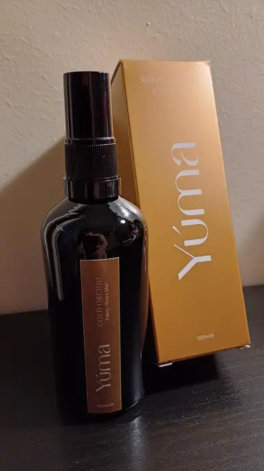 A black YUMA Gold Orchid Room Mist bottle next to its gold packaging.