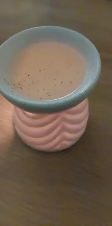 A ceramic oil burner with embossed patterns and melted wax with granules on the top dish.