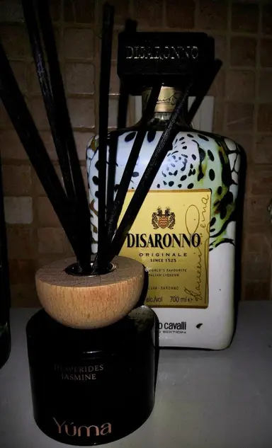 YUMA black room diffuser with a wooden cap and black reeds, positioned in front of a liqueur bottle.