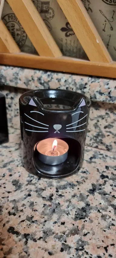 Black ceramic cat-shaped oil burner with a lit tealight inside, placed on a marble surface.