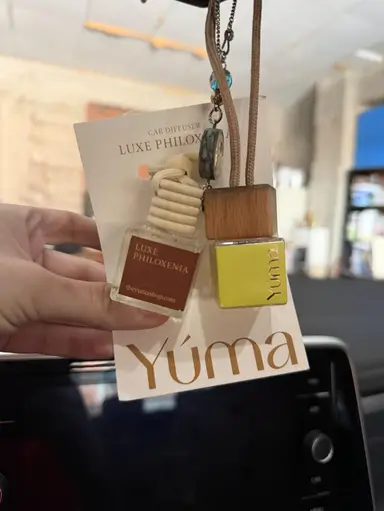 Two small YUMA glass car diffusers with wooden caps hanging in front of a white card.