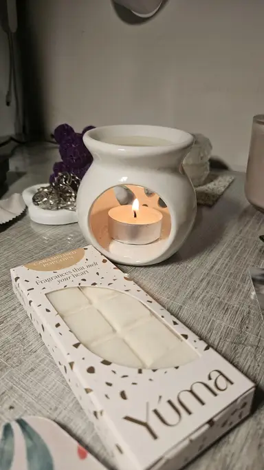 White ceramic burner with a lit tea light beside YUMA Caramelised Popcorn wax melt packaging.