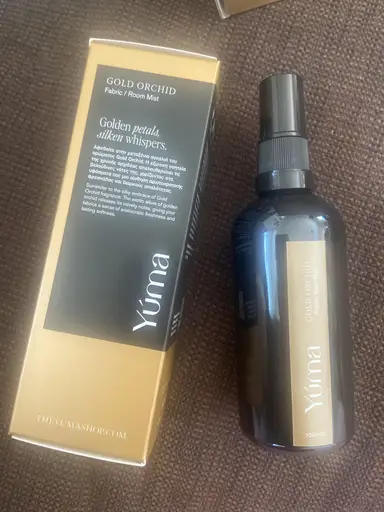 A YUMA Gold Orchid room spray next to its gold and black packaging.