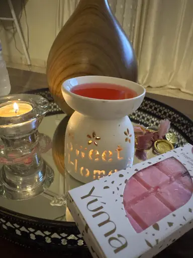 A white ceramic wax burner with melted pink wax next to a YUMA wax melt package.