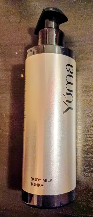 A YUMA Tonka Body Milk cylindrical bottle with a black pump against a dark background.