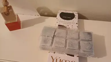 Grey wax melts in plastic packaging next to a YUMA car air freshener and a YUMA paper box.