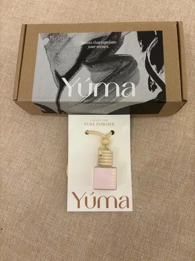 A YUMA Pure Powder car air freshener in front of its packaging box.
