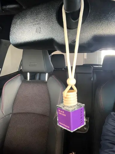 YUMA Black Orchid car air freshener hanging from the interior rearview mirror above the seats.
