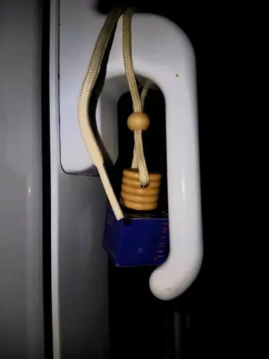 A small blue bottle with a wooden cap and cord hanging from a white window handle.