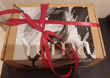 A YUMA paper gift box with black-and-white artwork, tied with a red satin ribbon.