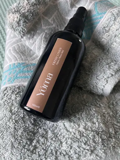 YUMA Fresh Linen Fabric Room Mist black bottle resting on a grey cotton towel.