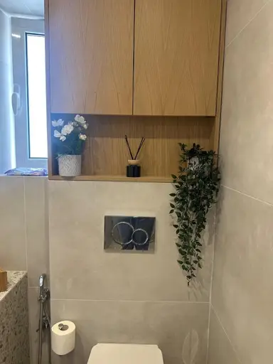 Wooden bathroom shelf styled with a reed diffuser, a pot of white flowers, and a decorative plant.