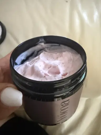 Open black YUMA jar with pink creamy contents and small dark granules.