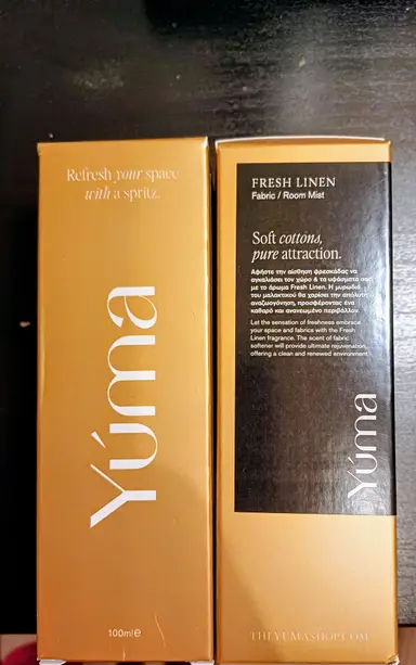 Two gold YUMA Fresh Linen Fabric Room Mist boxes on a black background.
