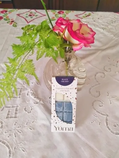 YUMA Black Orchid packaging next to a vase of roses on an embroidered white tablecloth.
