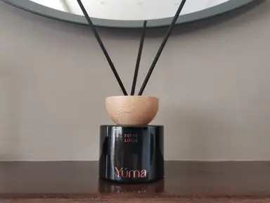 YUMA Fresh Linen black glass reed diffuser with a wooden cap and black reeds on a wooden surface.