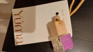 Small glass YUMA Car Diffuser Lilac Meadow bottle with a wooden cap and yellow cord.