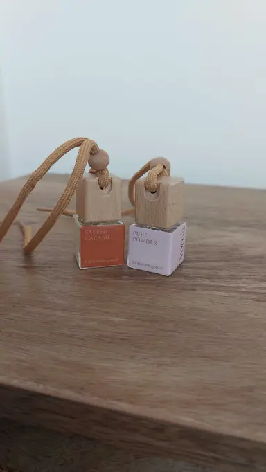 Two small YUMA glass car air fresheners with wooden caps and cords, placed on a wooden surface.