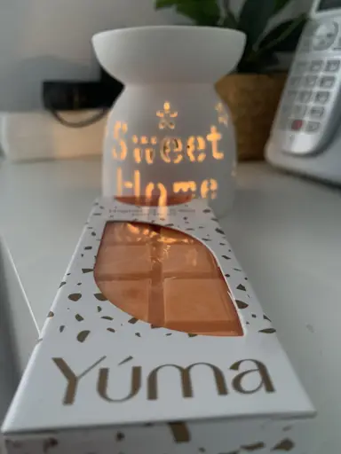 Orange YUMA wax melt in white packaging in front of a lit ceramic wax burner.