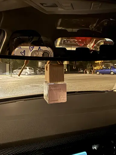 YUMA Pure Powder car diffuser hanging from the interior mirror with a road visible in the background.