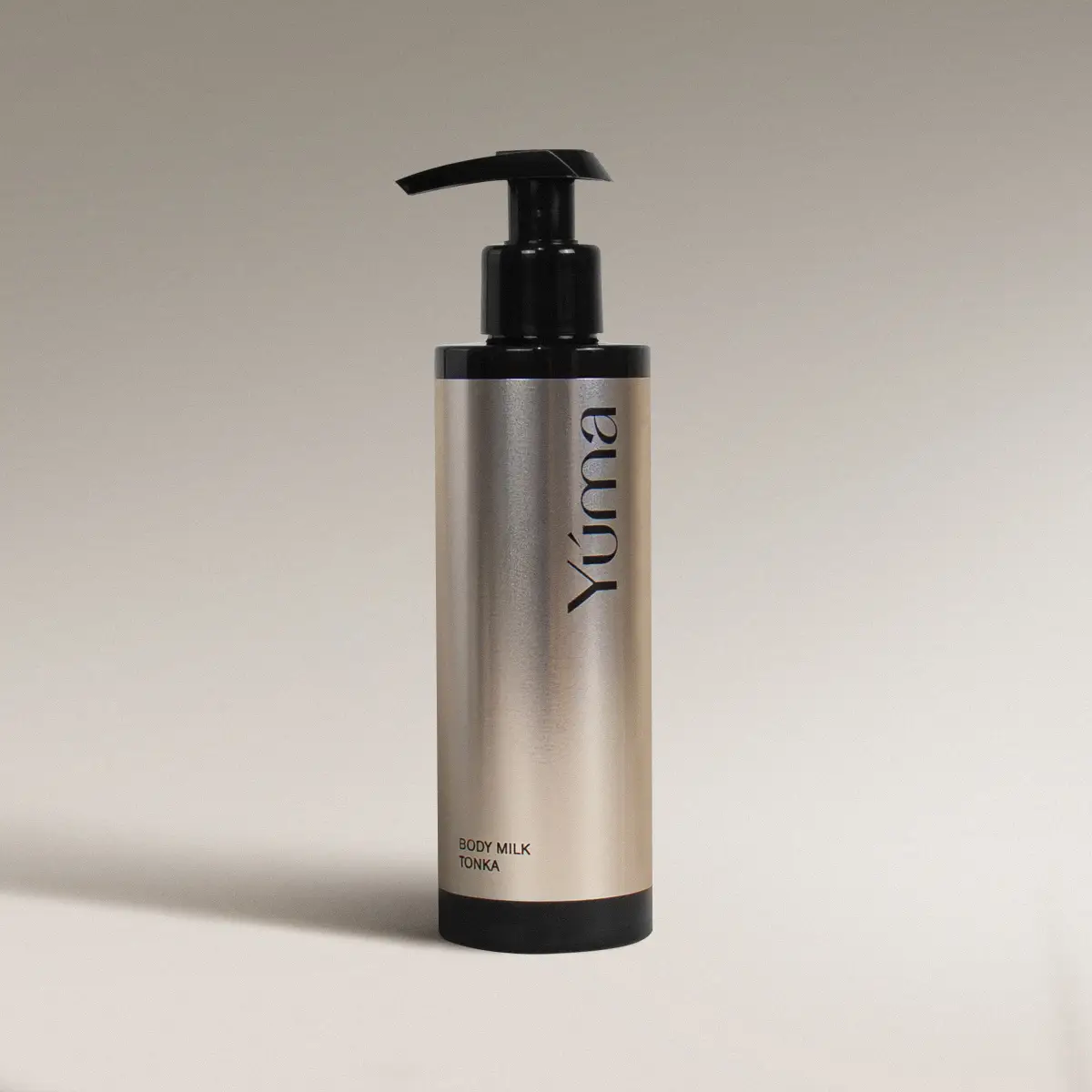YUMA Tonka Body Milk in a metallic bottle with a black pump, on a neutral background.