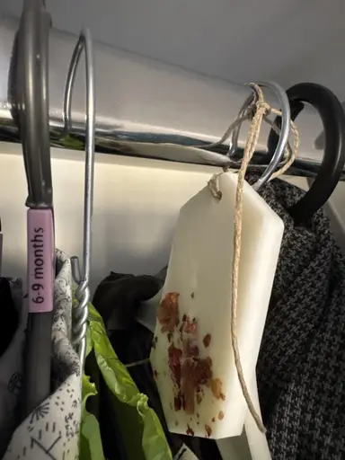 White wardrobe sachet with dried rose petals, hung by twine from a metal rod between clothing.