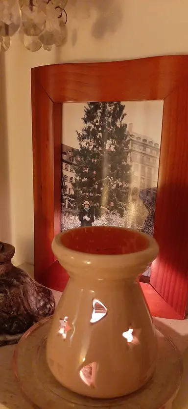A ceramic oil burner with star-shaped cutouts placed in front of a wooden frame holding a Christmas photograph.